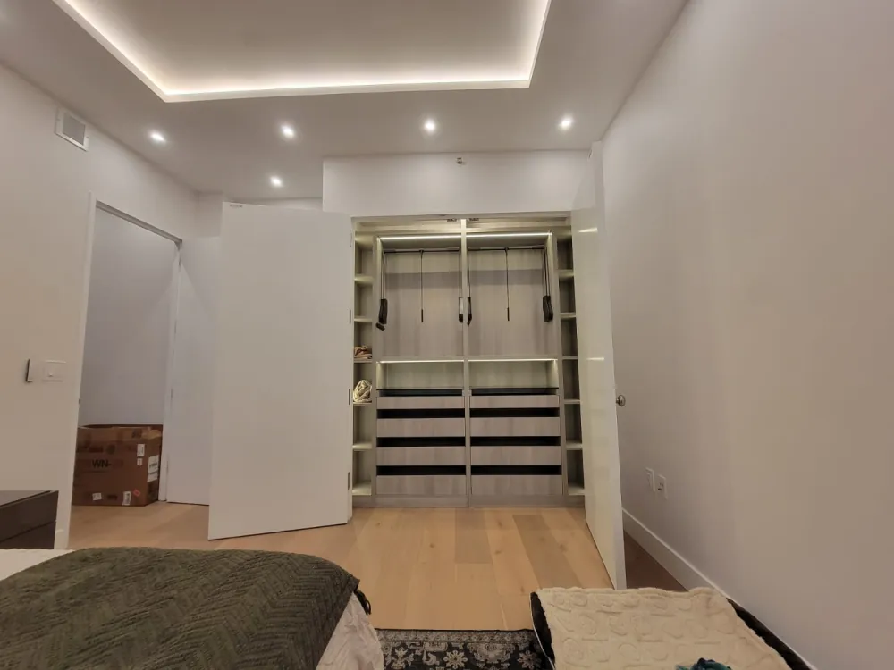 Built-in closet with pull-down hanging rods, LED-lit shelves and wood-grain drawers behind white double doors.