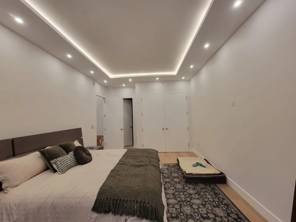 Bedroom with LED-lit tray ceiling, recessed lights, white double closet doors and light oak floor.