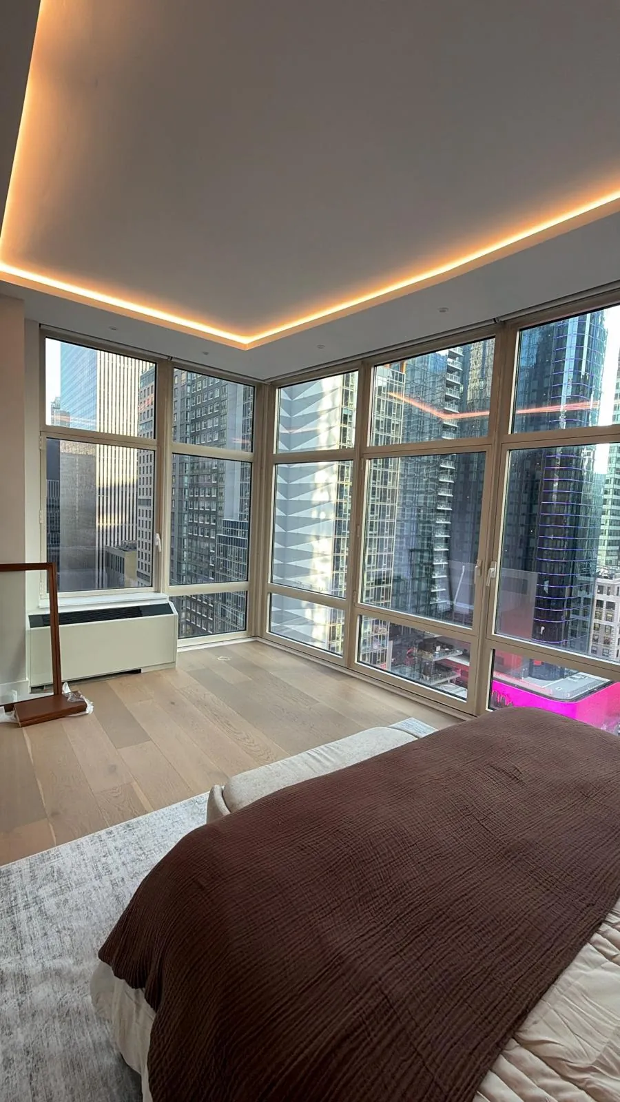Bedroom corner with glowing tray ceiling, wide plank oak floor and tall windows with city views.
