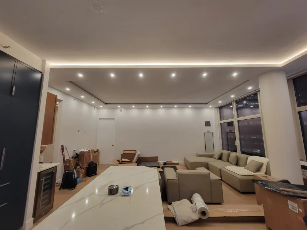 Open living room with LED cove ceiling and recessed lights, sectional sofa and moving boxes during final setup.
