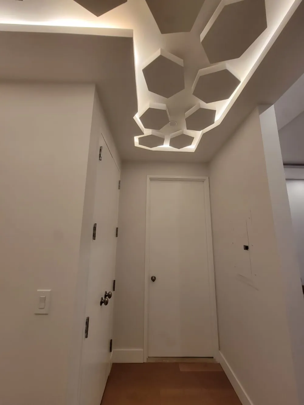 Entry hall with hexagon drywall ceiling panels glowing with hidden LED light above white flush doors.