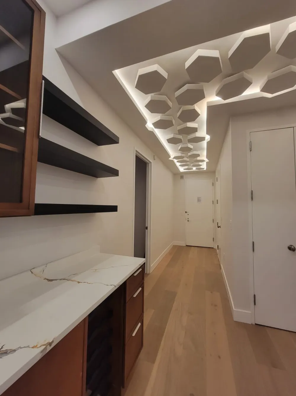 Hallway with hexagon drywall ceiling and hidden LED lighting beside a wet bar with floating shelves and quartz top.