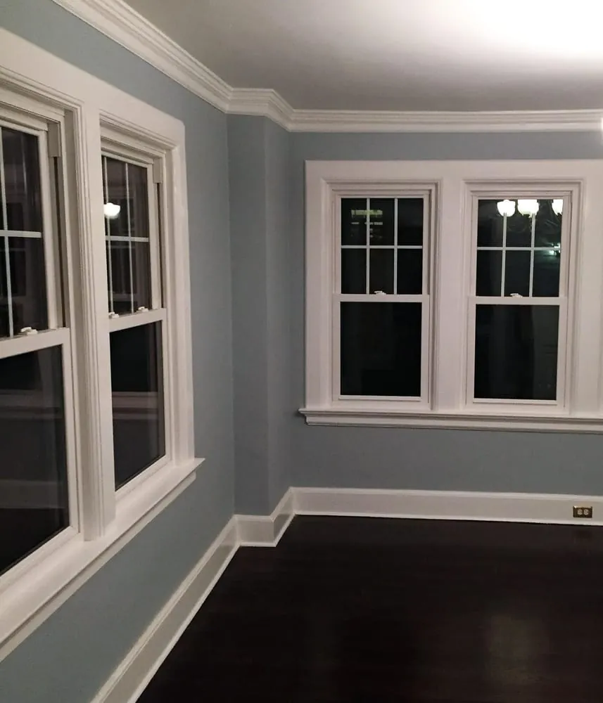 Room with blue-gray walls, white crown molding, wide window casings, baseboards and dark stained hardwood floor.