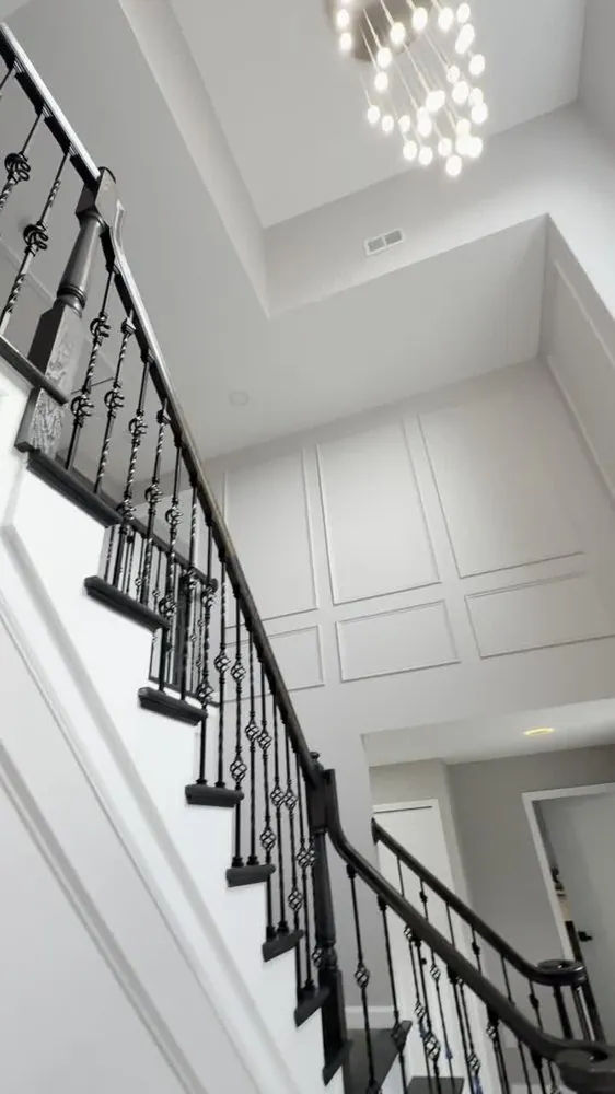 Two-story foyer staircase with dark rail, black twisted iron balusters, white panel molding and a bubble chandelier.