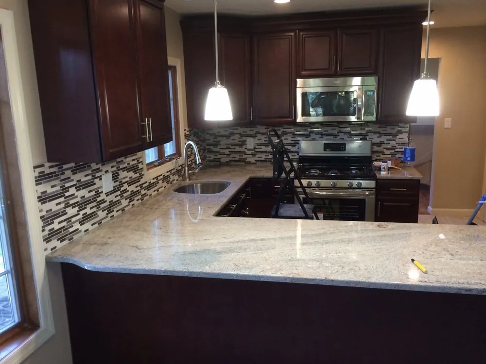 Cherry cabinet kitchen with light granite peninsula, brown and white mosaic backsplash, stainless range and two pendants.