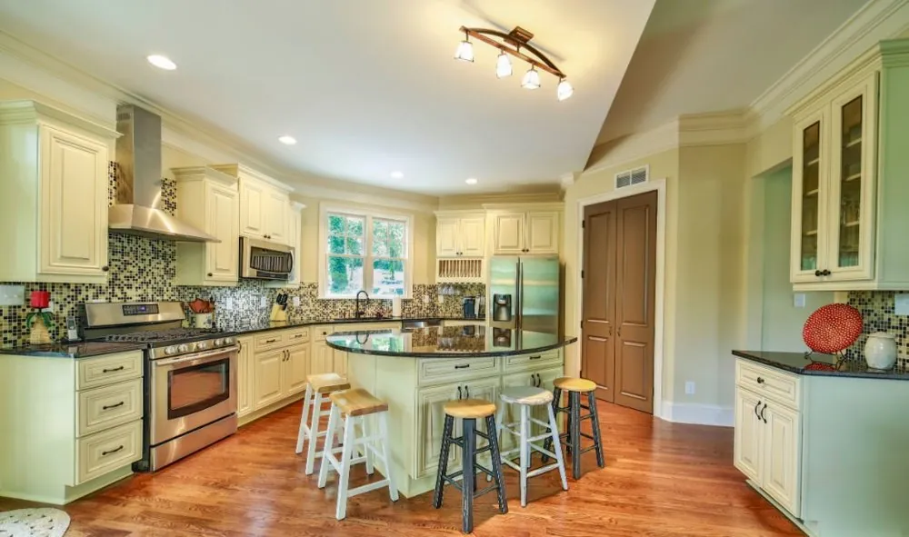 Kitchen with cream raised-panel cabinets, black granite counters, mosaic backsplash, round island with stools and oak floor.