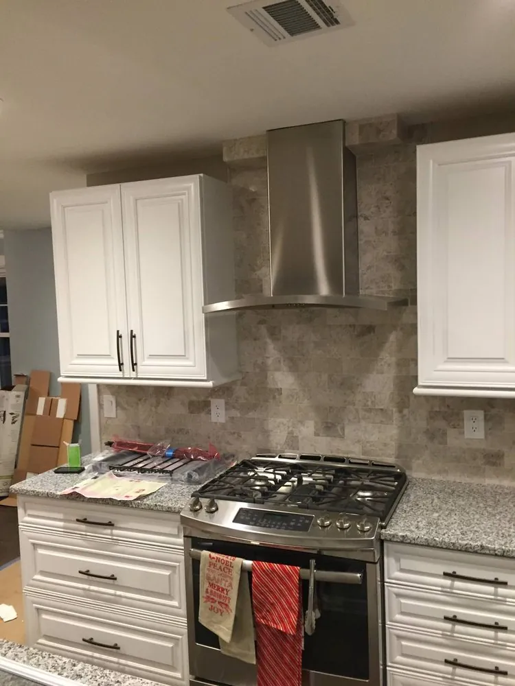 White raised-panel cabinets, travertine subway backsplash, chimney hood and gas range, with boxes still on the floor.