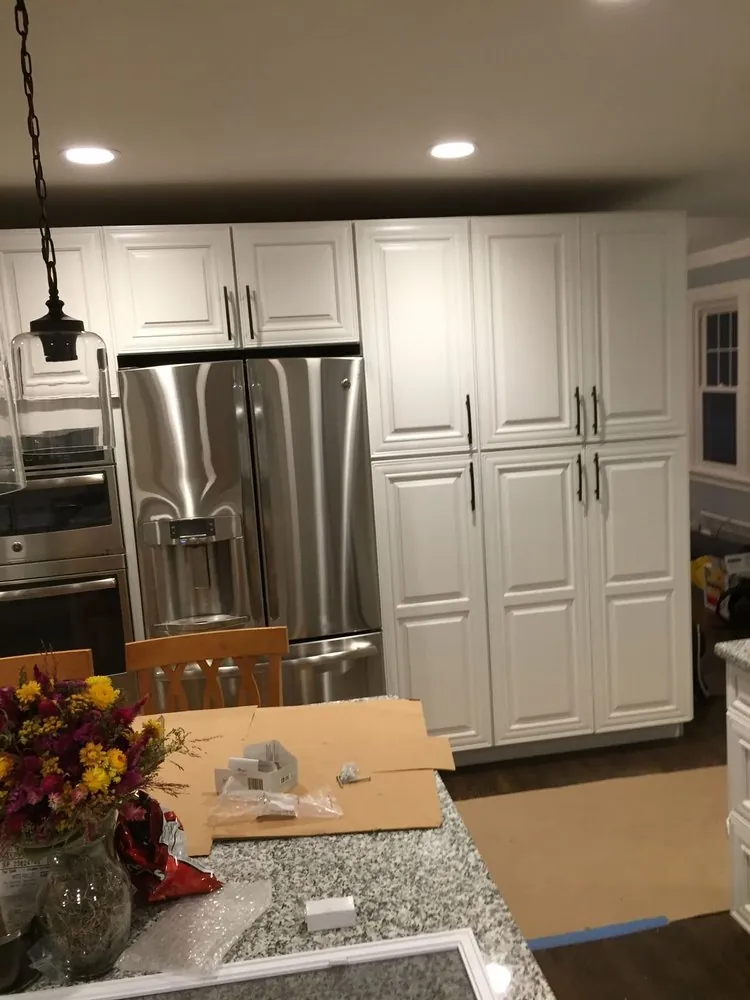 White raised-panel pantry wall with stainless fridge seen past a granite island covered in cardboard and packing.