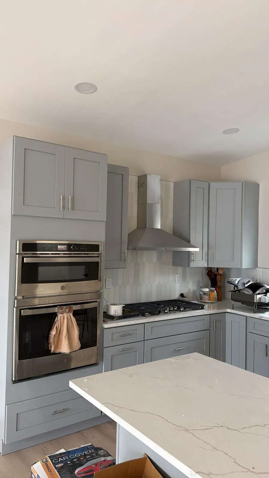 Kitchen with gray shaker cabinets, stainless wall ovens and chimney hood, white picket tile backsplash and quartz island.