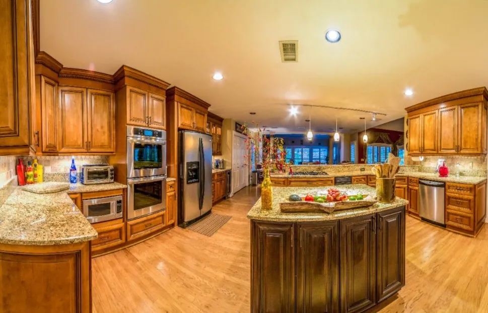 Large kitchen with maple cabinets, granite counters, double wall oven, stainless fridge and a dark wood island with fruit.