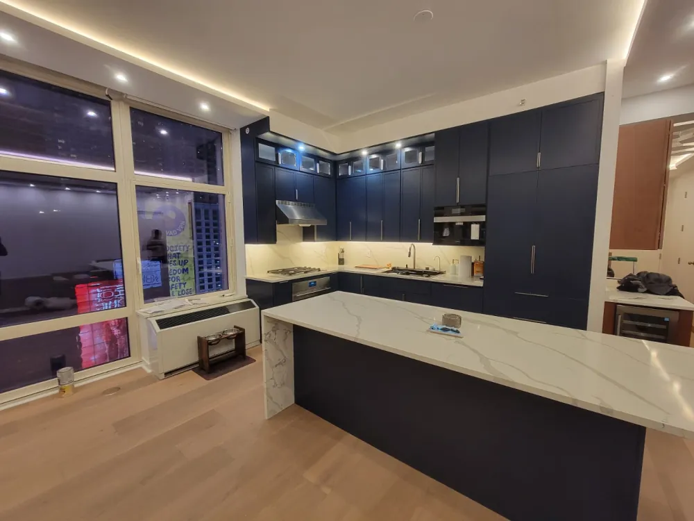 Kitchen with navy shaker cabinets, glass-front uppers and a long white quartz waterfall island on a light oak floor.