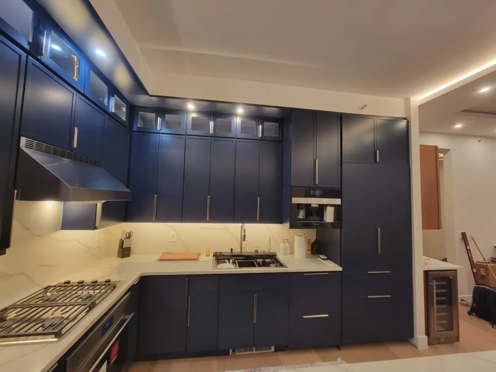 Kitchen with navy shaker cabinets to the ceiling, glass-front uppers, quartz slab backsplash and stainless hood.