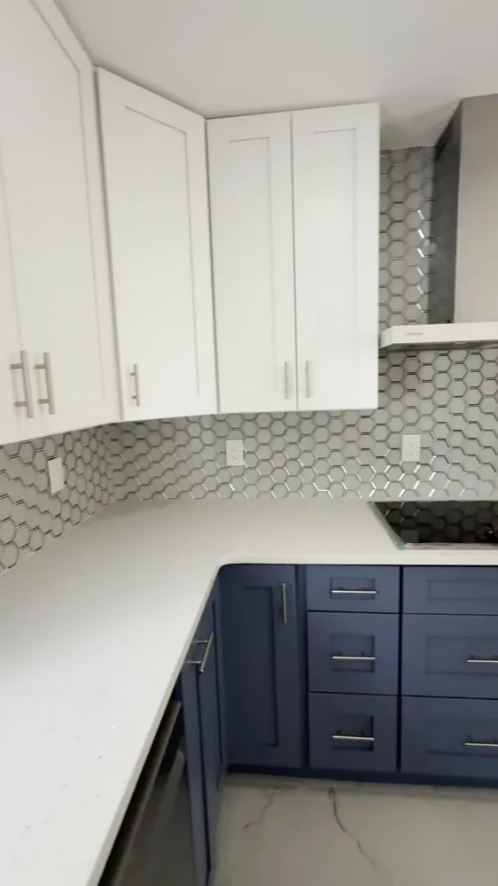 Kitchen corner with white upper and navy lower shaker cabinets, white quartz counters and a gray hexagon tile backsplash.