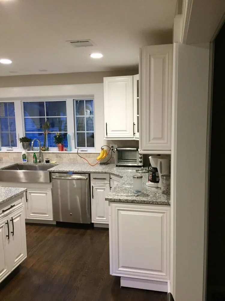 White raised-panel kitchen with stainless farmhouse sink, gray granite counters, dishwasher and windows over the sink.