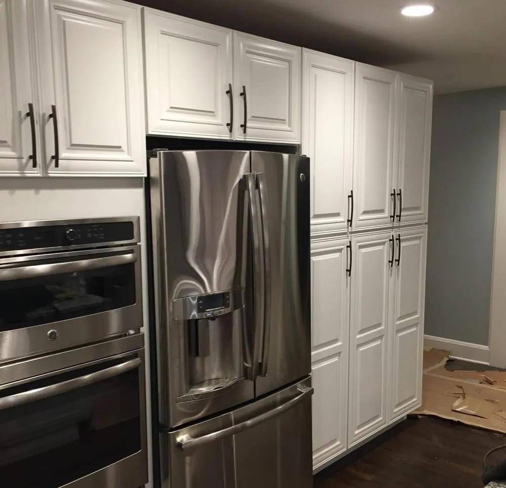 Wall of white raised-panel pantry cabinets around a stainless French-door fridge and double wall ovens.