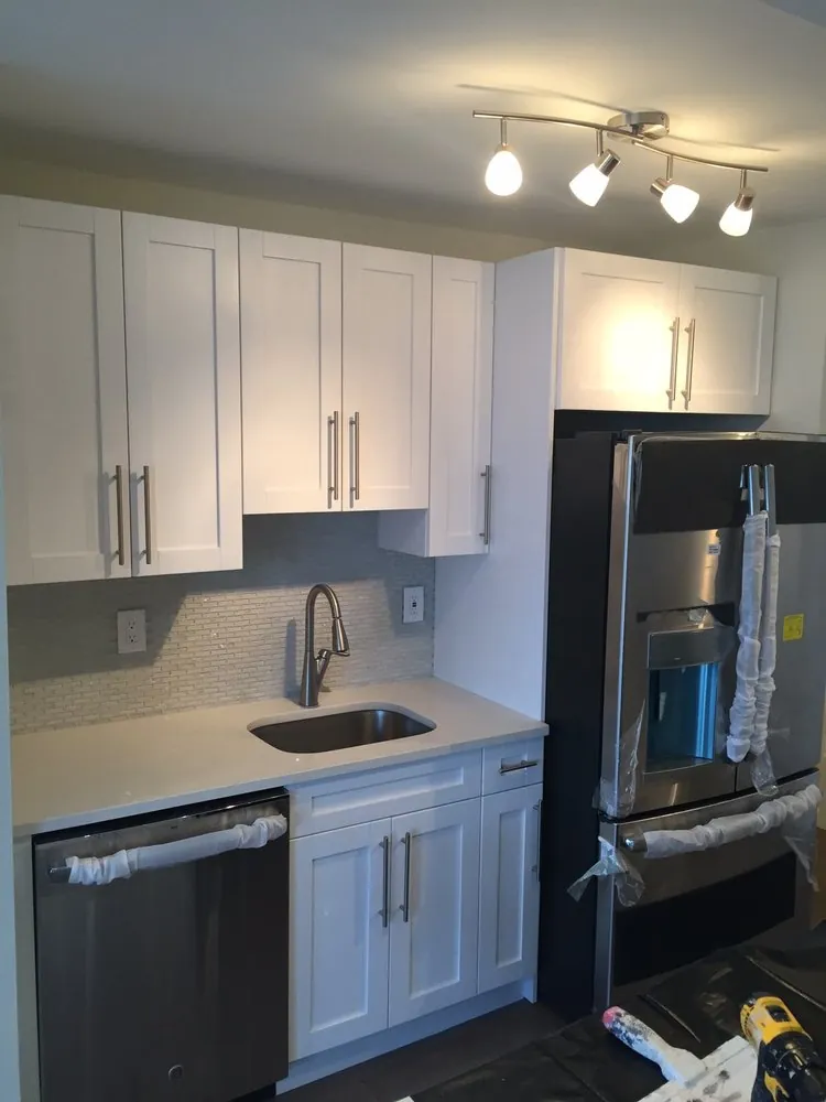 White shaker cabinets with quartz counter, undermount sink, glass mosaic backsplash and a new fridge still wrapped.