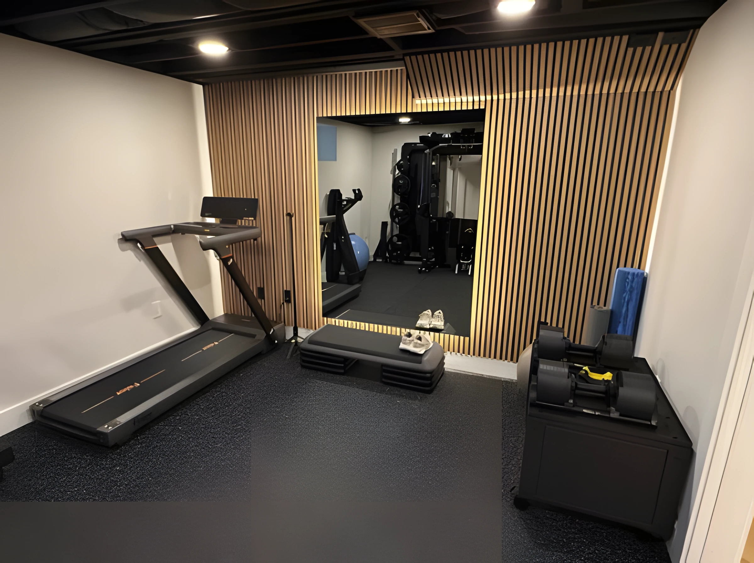 Basement home gym with a wood slat accent wall, a mirror, rubber flooring and a treadmill