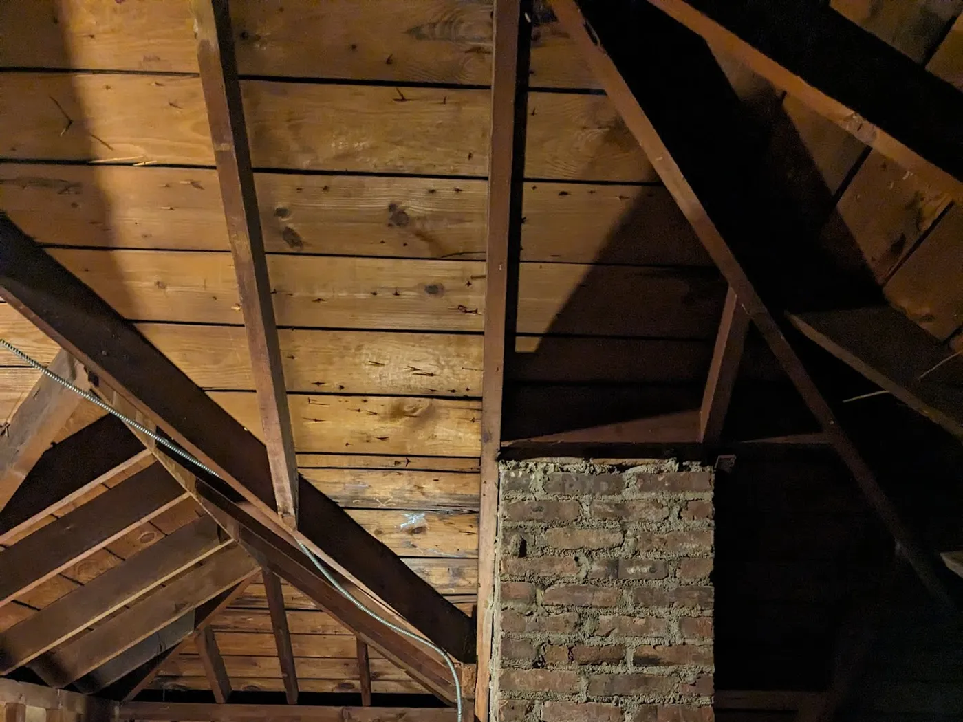 Unfinished attic with exposed rafters, board roof sheathing, a brick chimney and a gable-end window